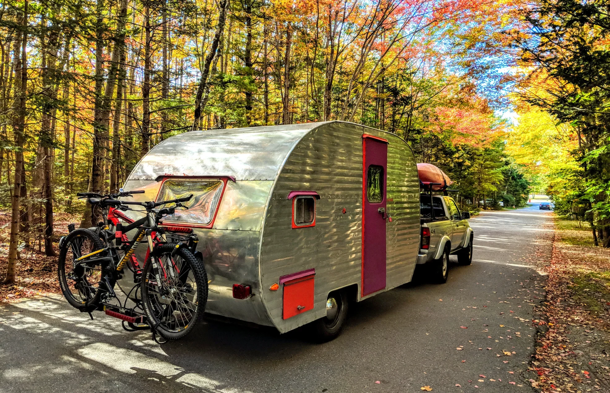 Camping trailer driving into the Bar Harbor Campground through a forest of fall foliage.