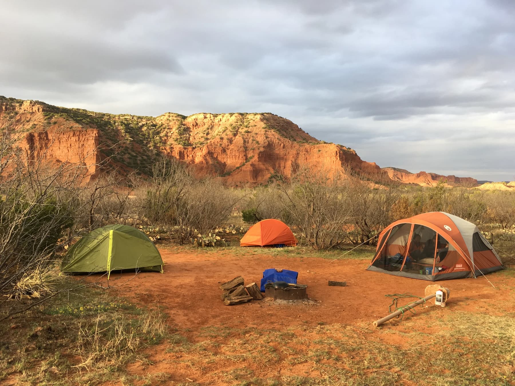 Three tents pitched at a desert campsite surrounded by red rock walls covered in sage brush.