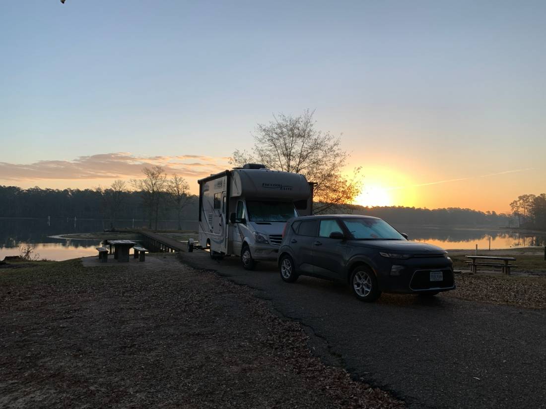 Class C motorhome and tow vehicle set up in back-in site alongside a lake