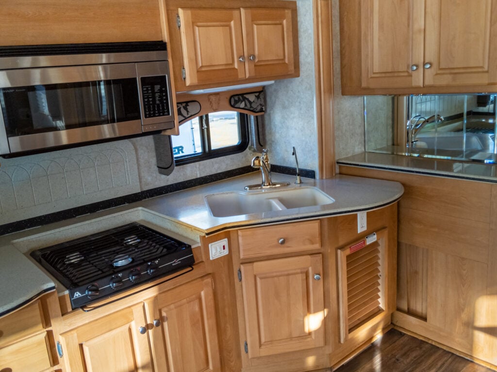 an RV kitchen area with a sink, stove, microwave, cabinets and a microwave in the corner of the room, image for RV kitchen organization tips 