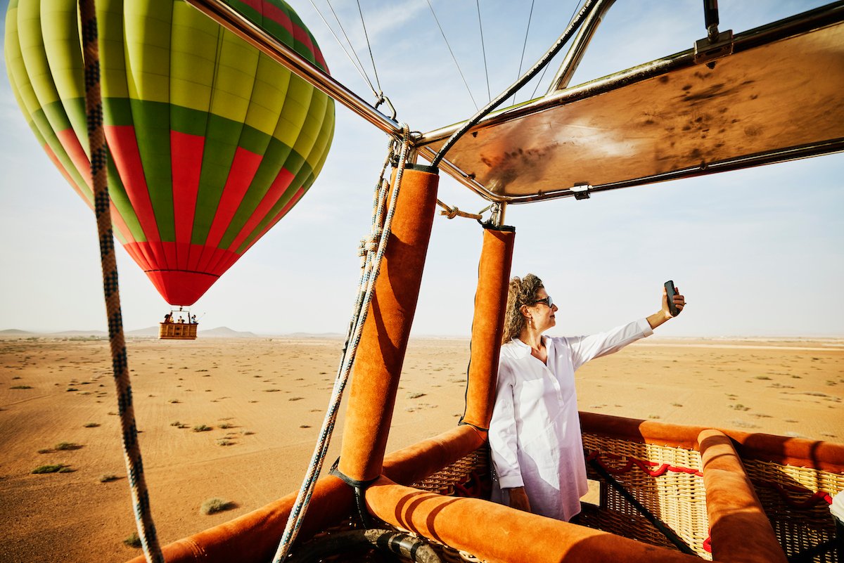 Wide shot woman taking selfie during sunrise hot air balloon ride