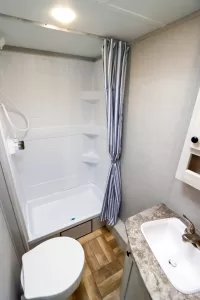 The rear bathroom has a plastic shower, a pedal-flush toilet, and a vanity.
