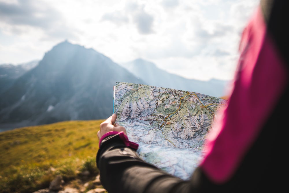 a woman holding a topographic map in front of a mountain at dawn