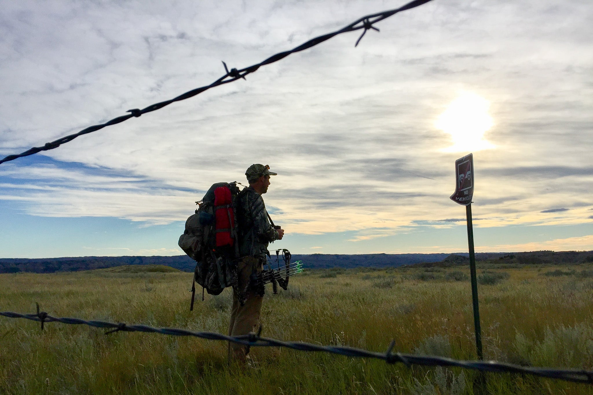 Hunter stands between barbed wire and sign of closed lands.