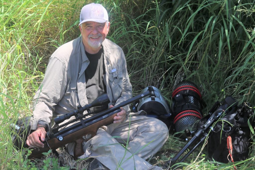 A man crouched in grass holding a gun