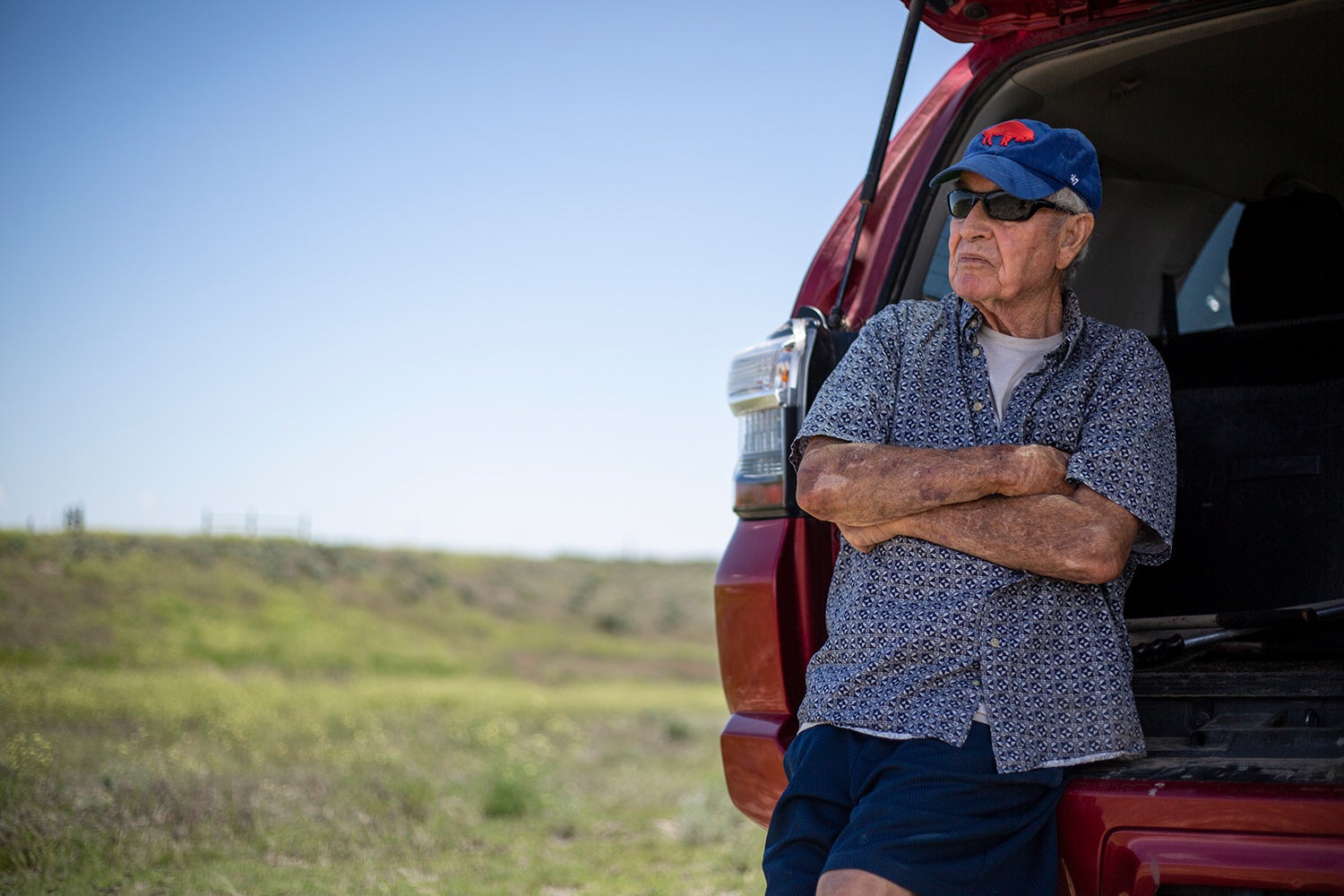 man leans on open back of car, gazes out onto prairie