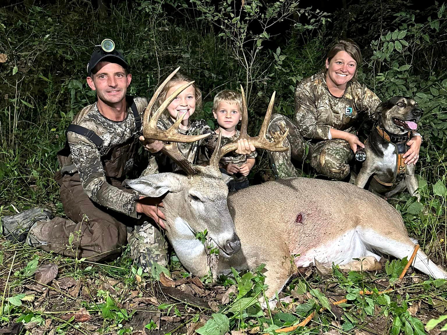 A family and their tracking dog sit behind a big buck.
