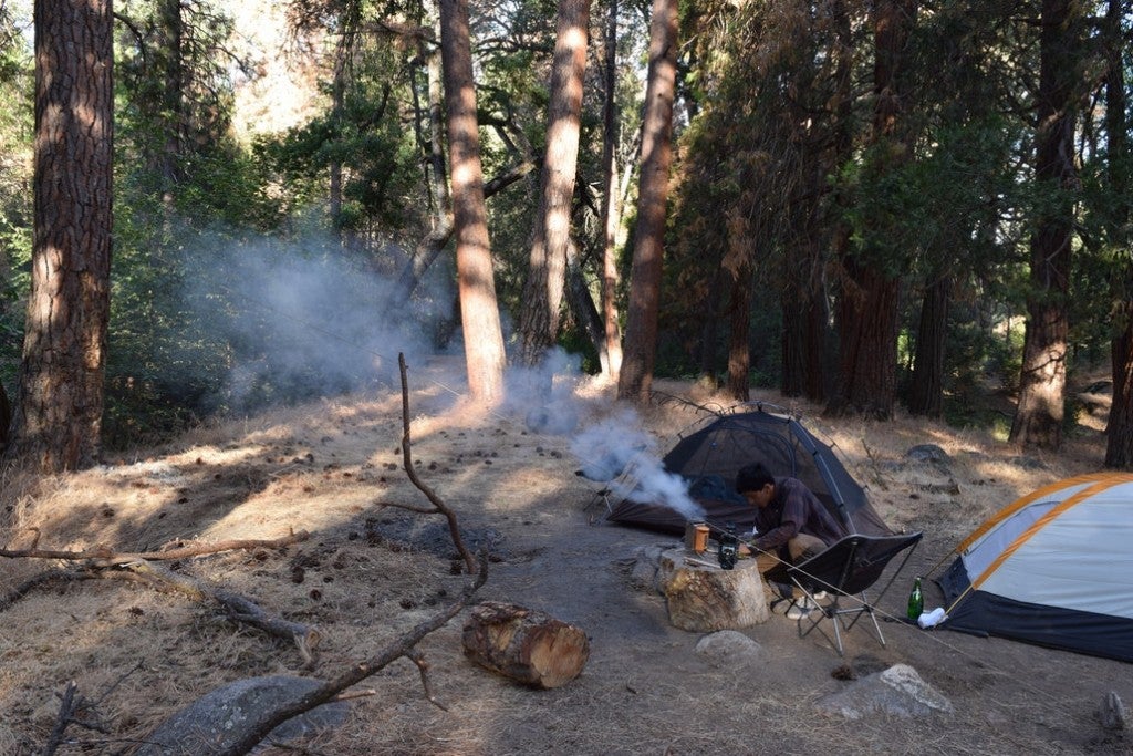 a campsite in the woods with a tent and a man cooking over a fire