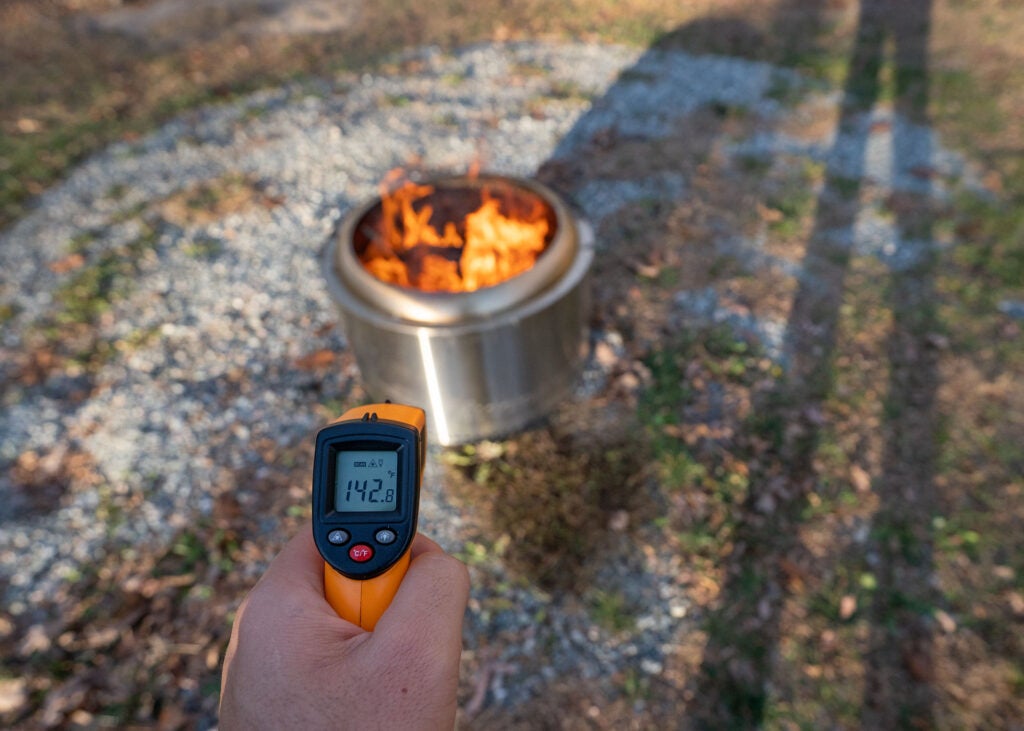 A hand holding a laser thermometer over the Solo Stove fire pit.