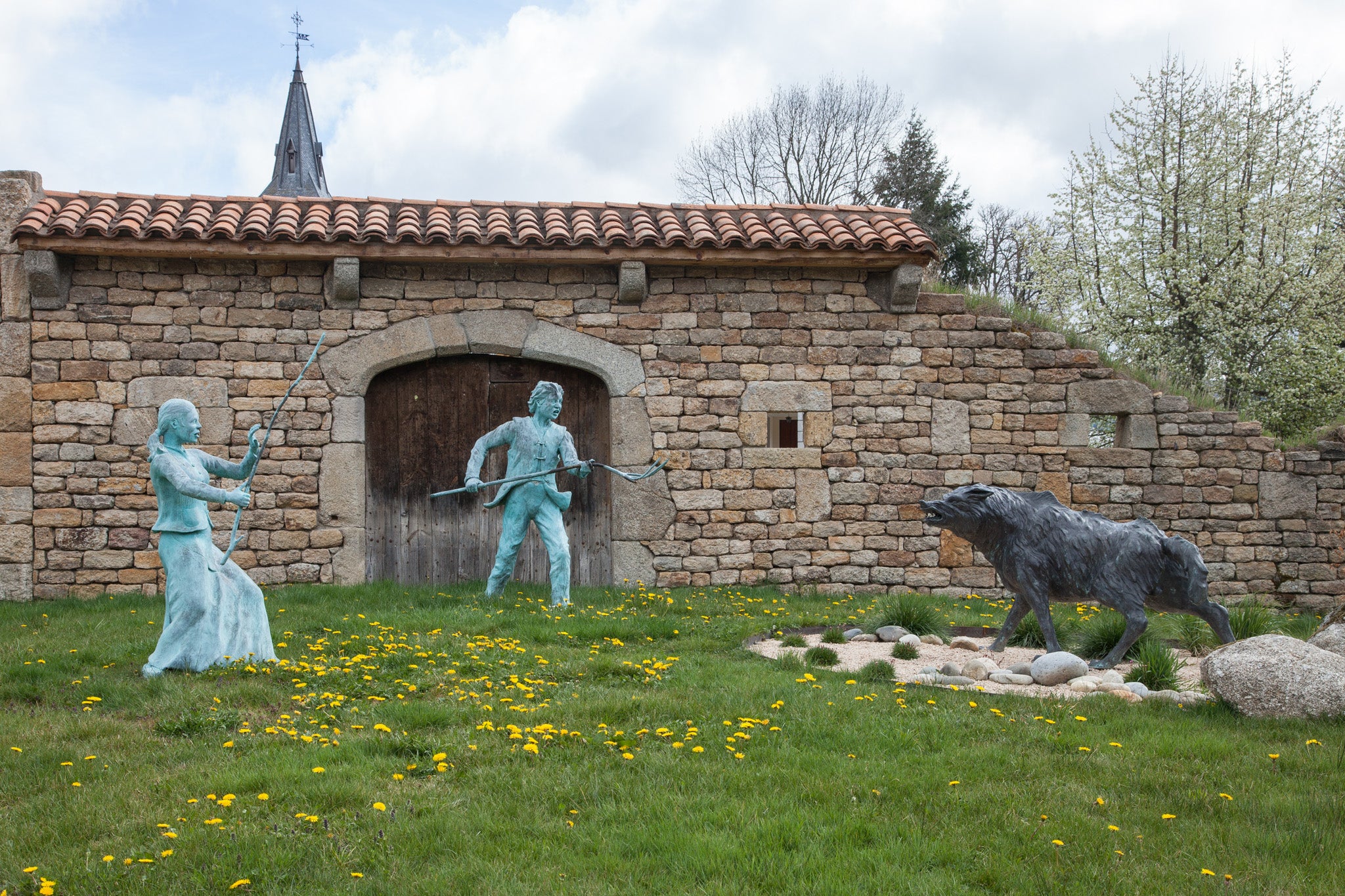 Two copper statues of peasants defend themselves from the Beast of GÃ©vaudan.