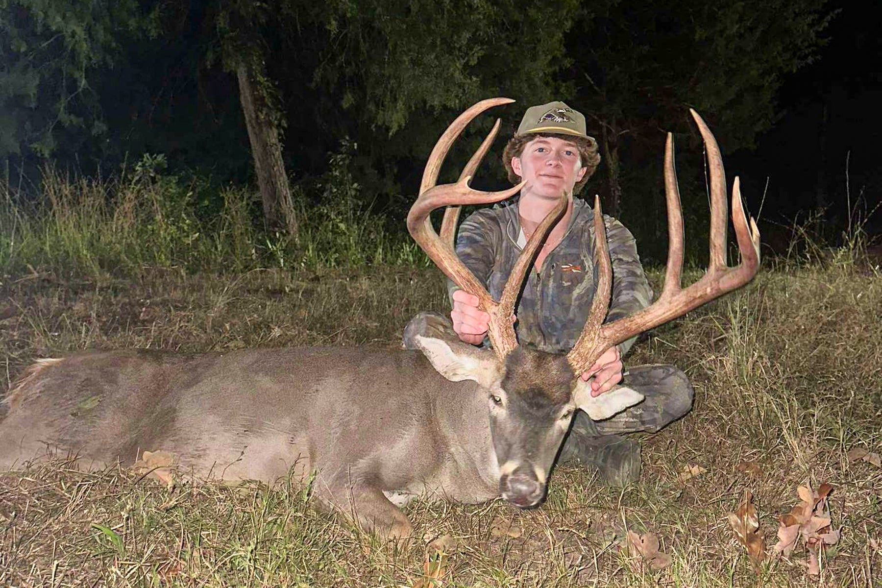 A teenager sits behind a big 10-point buck.