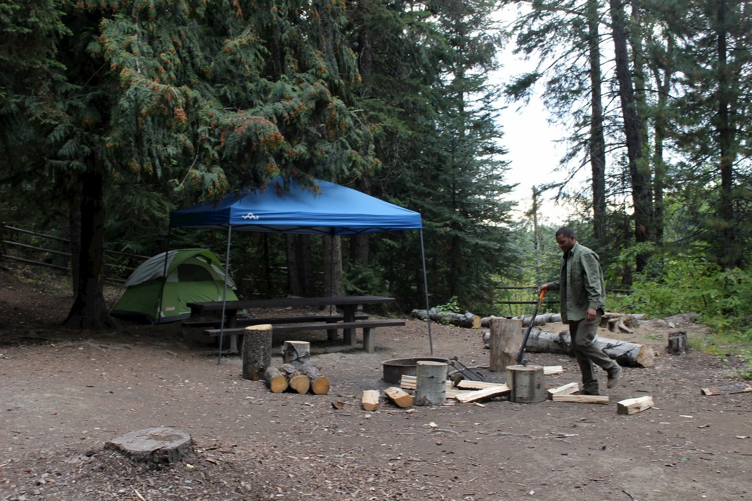 Camper chopping wood beside a fire pit at campsite.