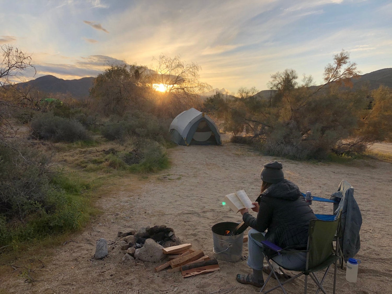 woman reading book by campfire with tent in the background