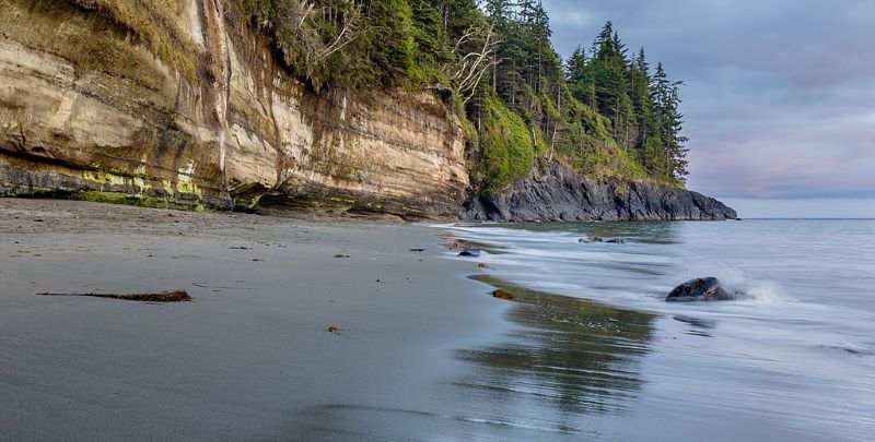 Canadian West coast with dark sand beach and rugged cliffs