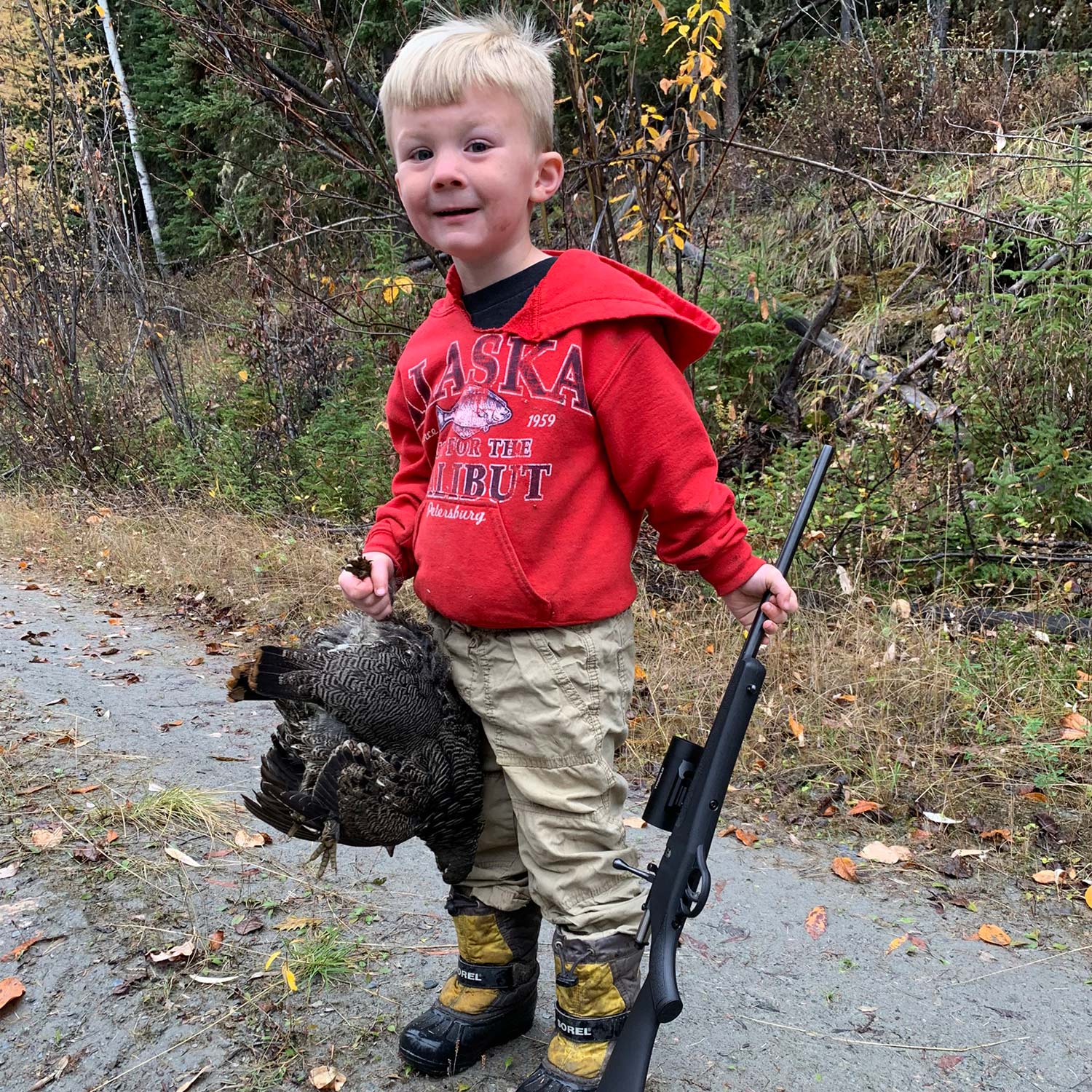 A young child holding up a spruce grouse.