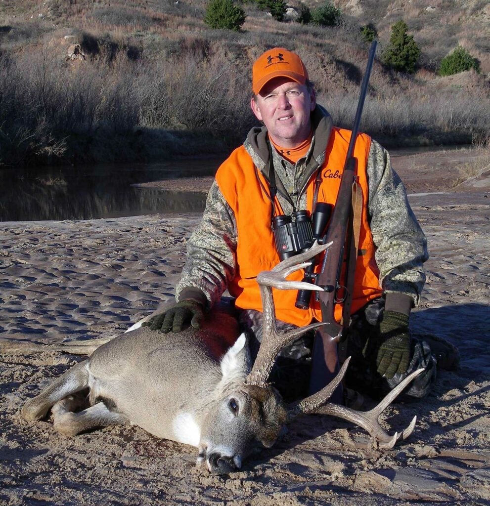 hunter kneeling behind a whitetail buck.