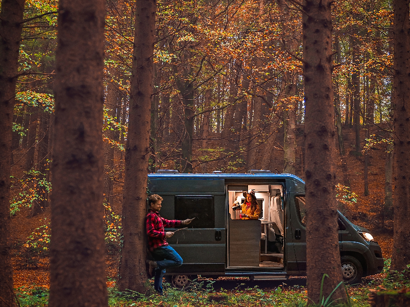 Camper van parked in the forest with a female inside and a male outside - green RVing