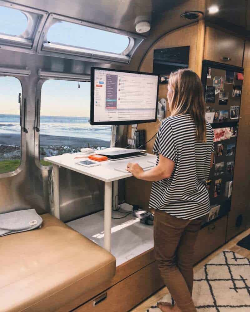 Lady standing at a desk in an Airstream looking out the window at the ocean - internet for RVing