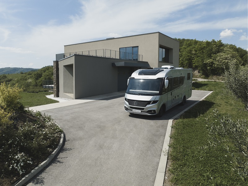Large Class A Adria Motorhome parked outside a very modern European home in a rural setting