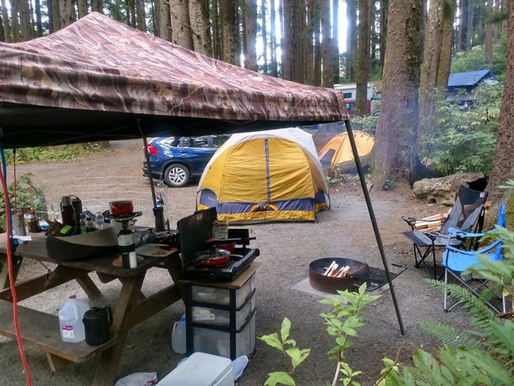 a tent and picnic table set up with camping gear near a forest