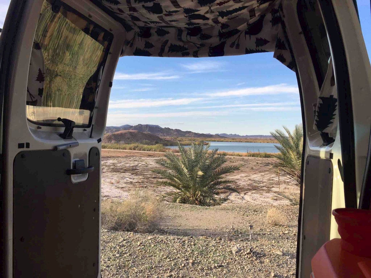 View through camper of tropical plants, desert, and lake.