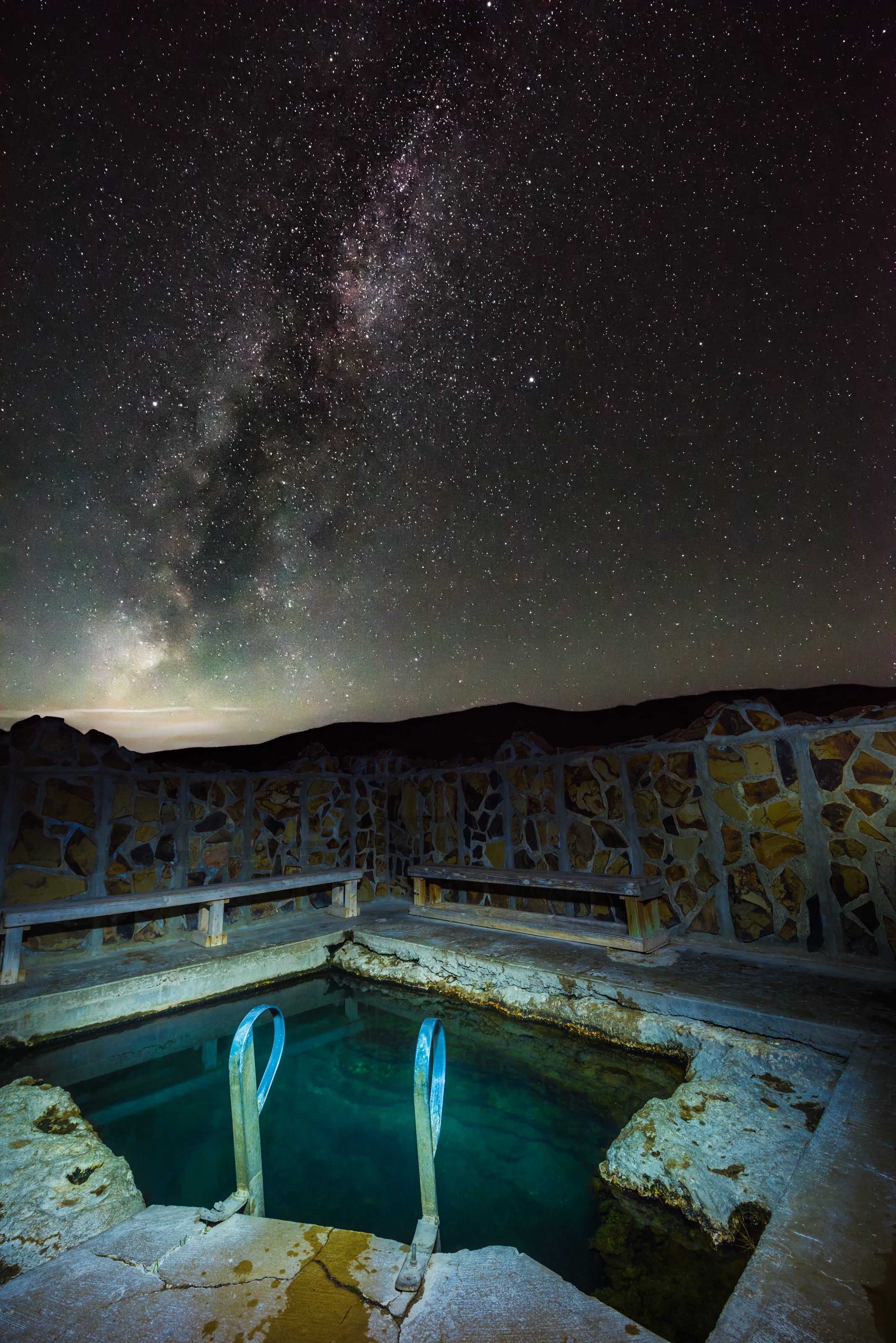 Hot springs at night under the star filled sky with a ladder and brick pool.