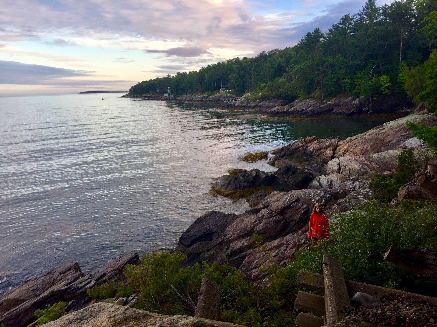 Girl in red jacket walking along coastal cliffs in Maine.