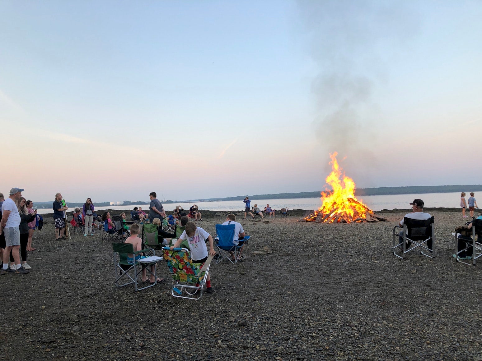 Beach bonfire surrounded by campers in beach chairs.