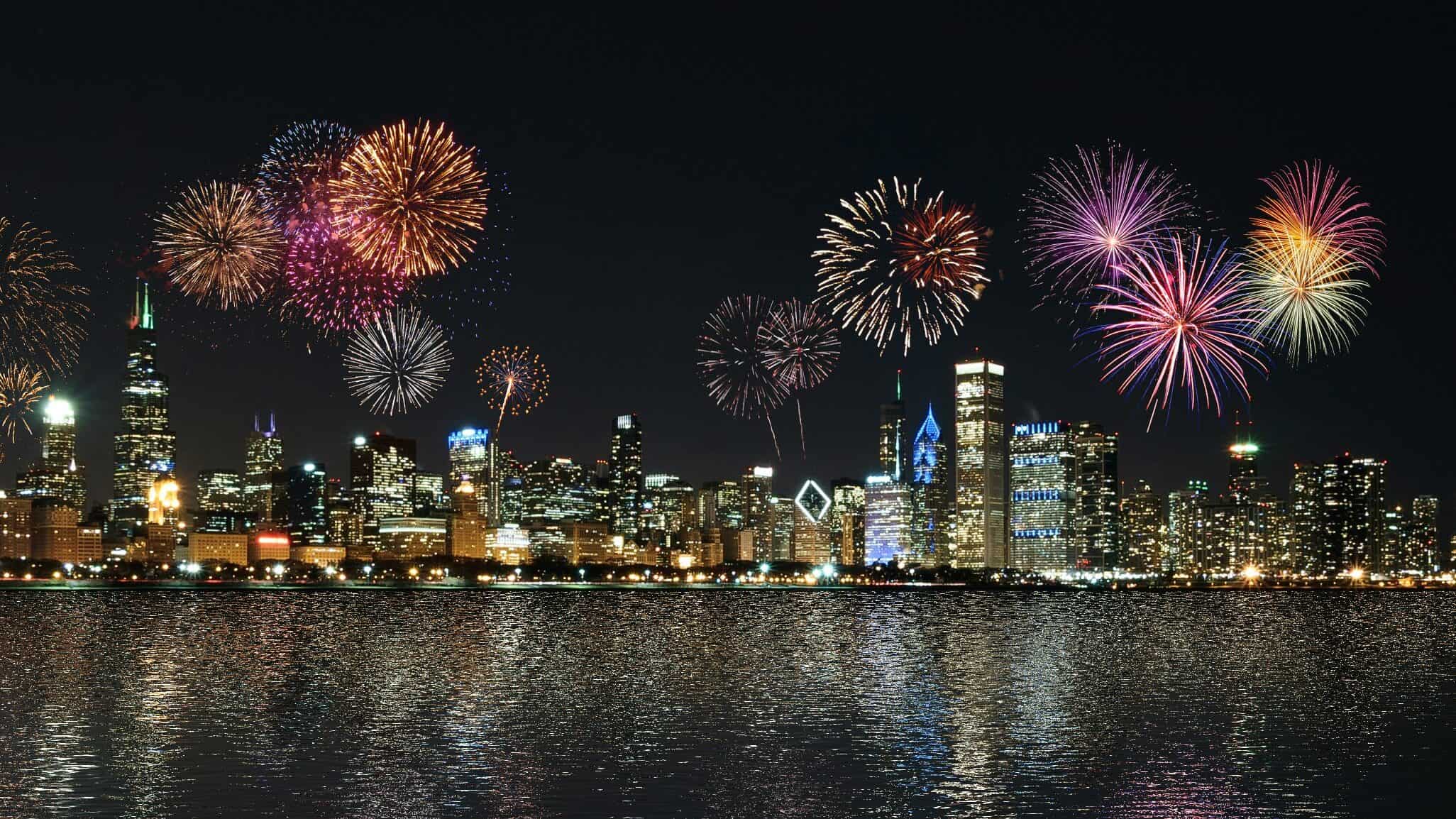 A colorful Fourth of July fireworks display over a cityscape in front of a harbor.