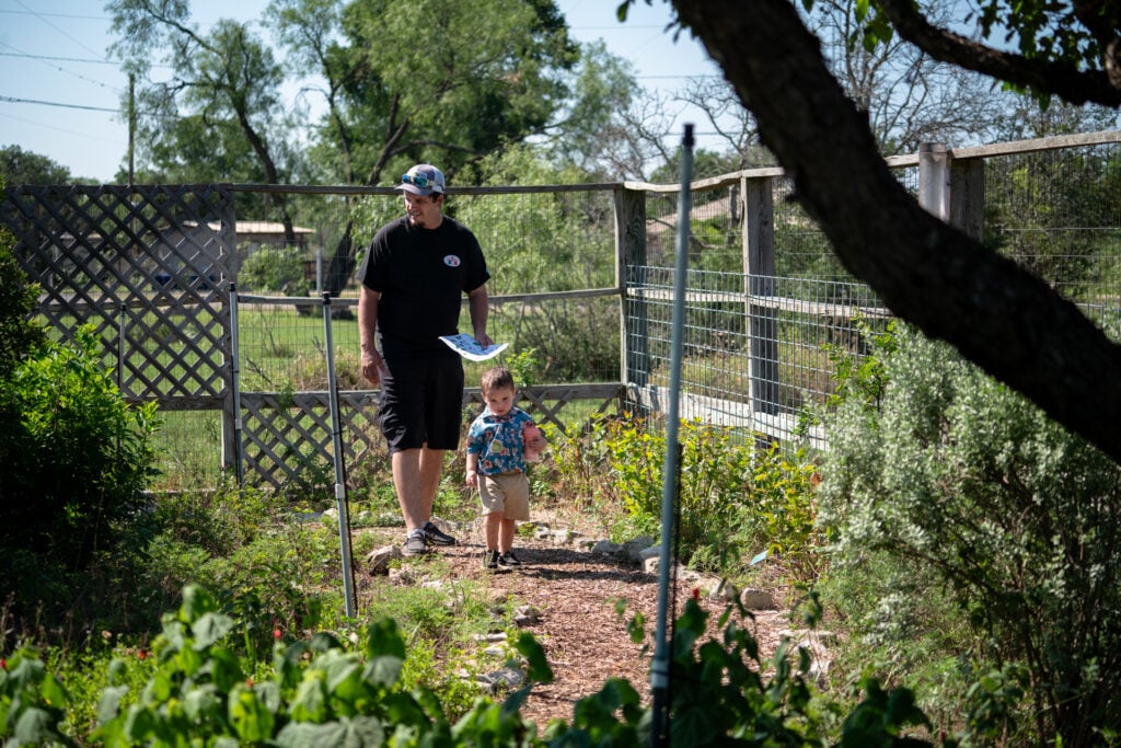 Man and young son walk through a fenced garden in Kerrville Texas.