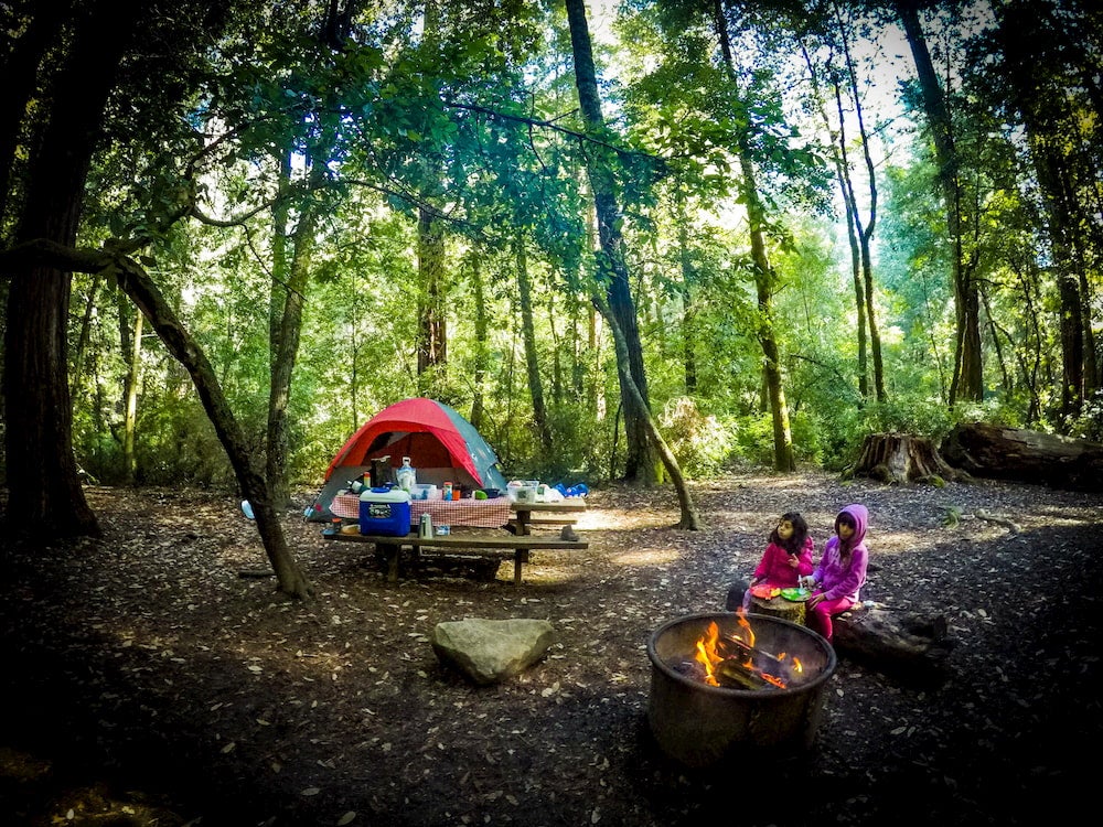 Campsite with two young girls sitting around campfire while camping in Santa Cruz county, California