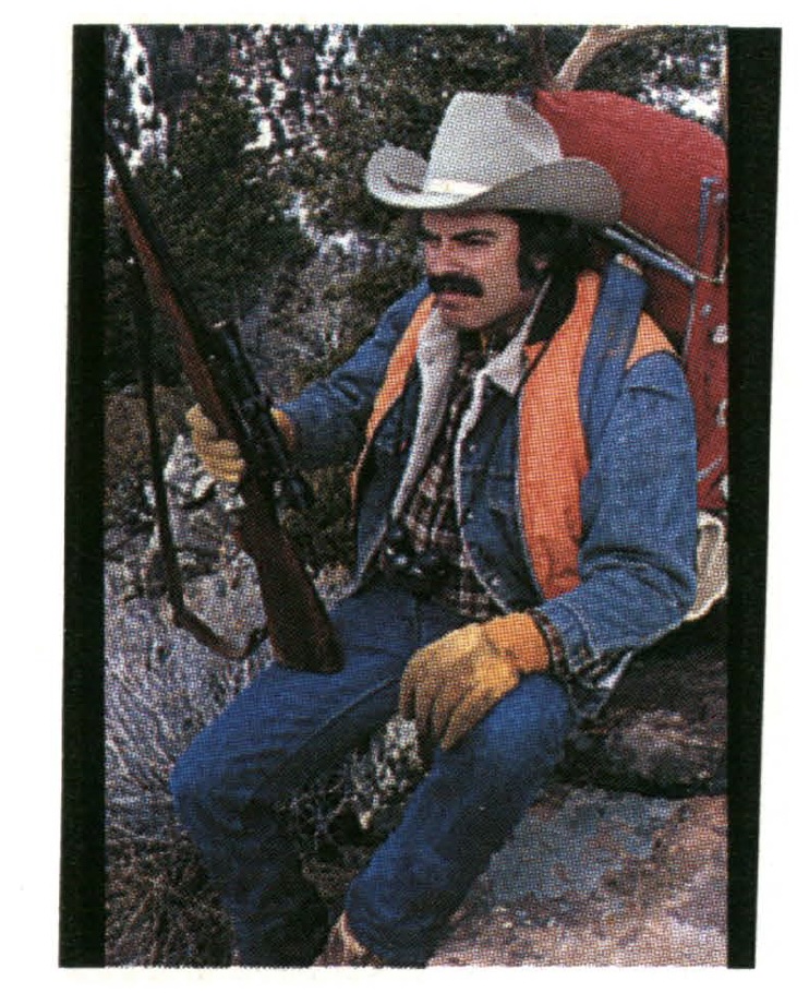 Jim Zumbo in denim and blaze orange, holding a wood stocked deer rifle.