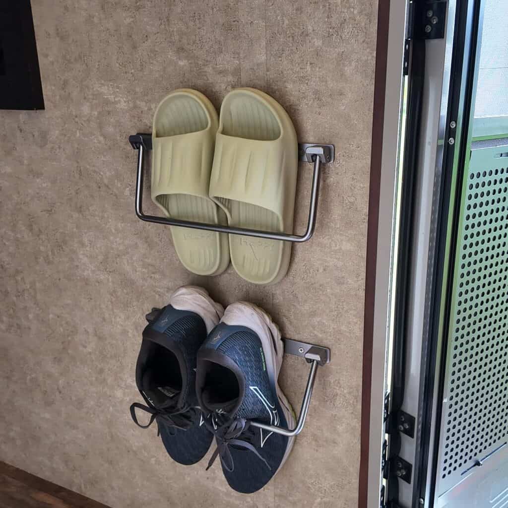 Wall-mounted foldable shoe rack holding two pairs of shoes in an RV living area.