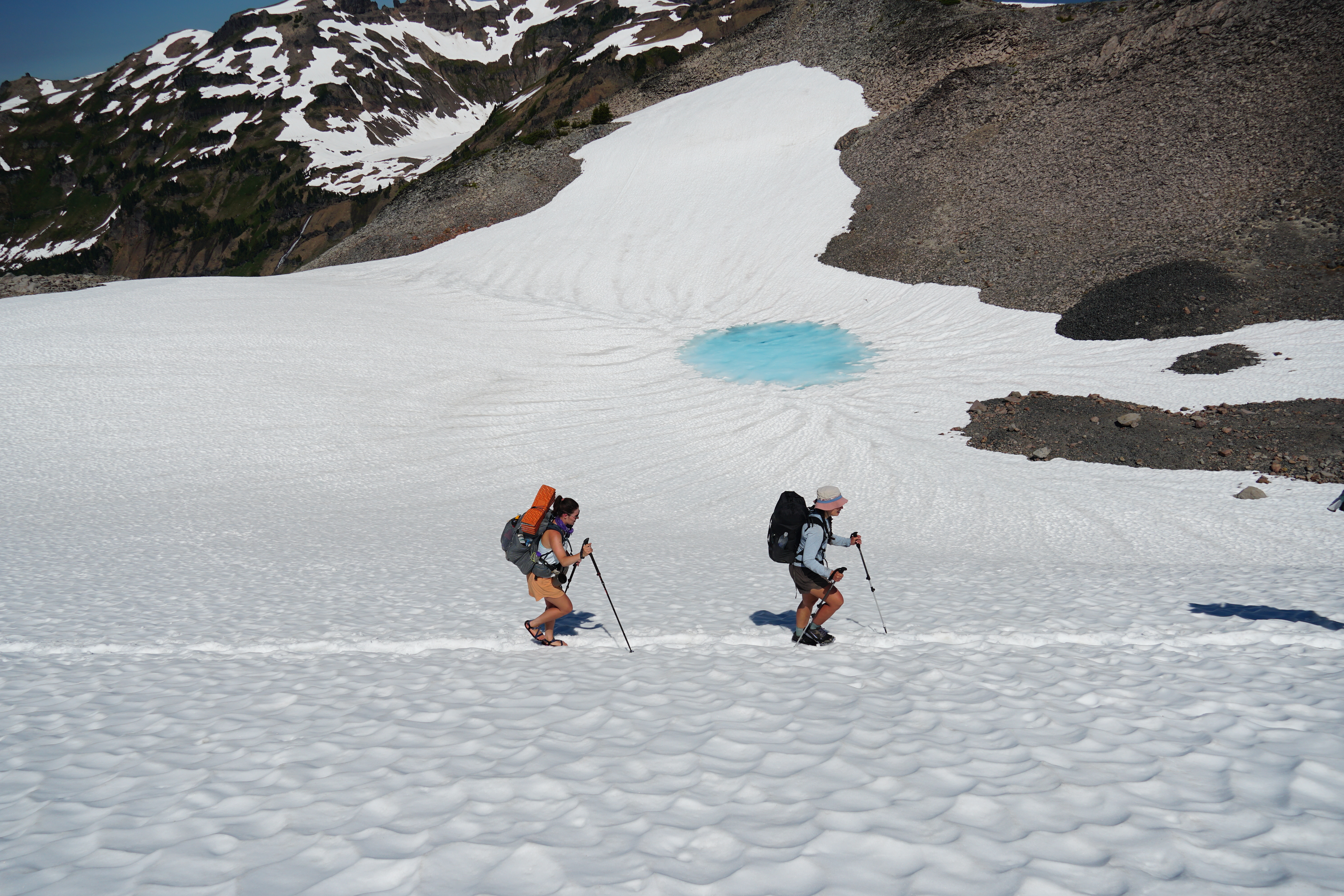 Backpackers traverse snowfield.