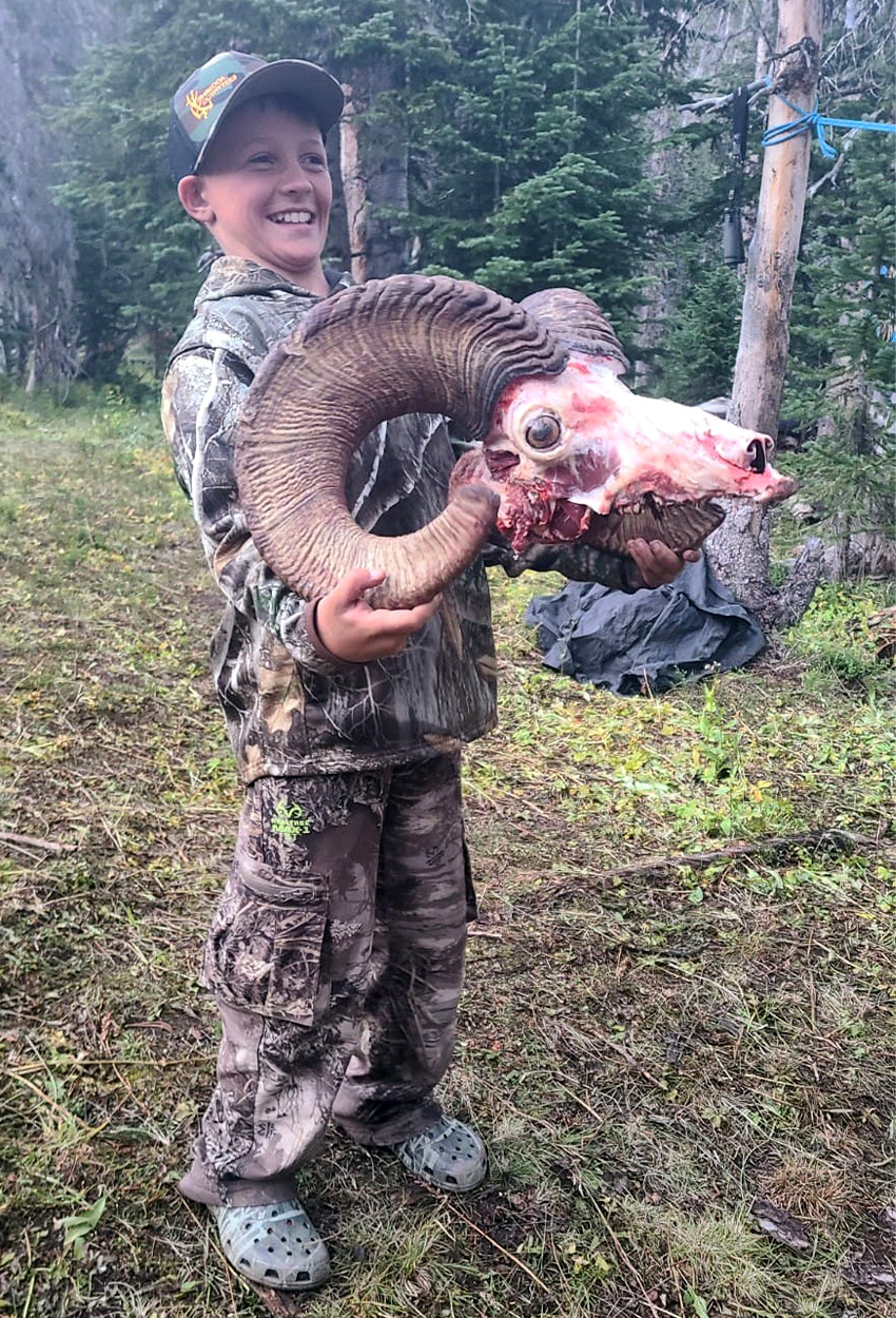 A young hunter holds up a bighorn ram skull.