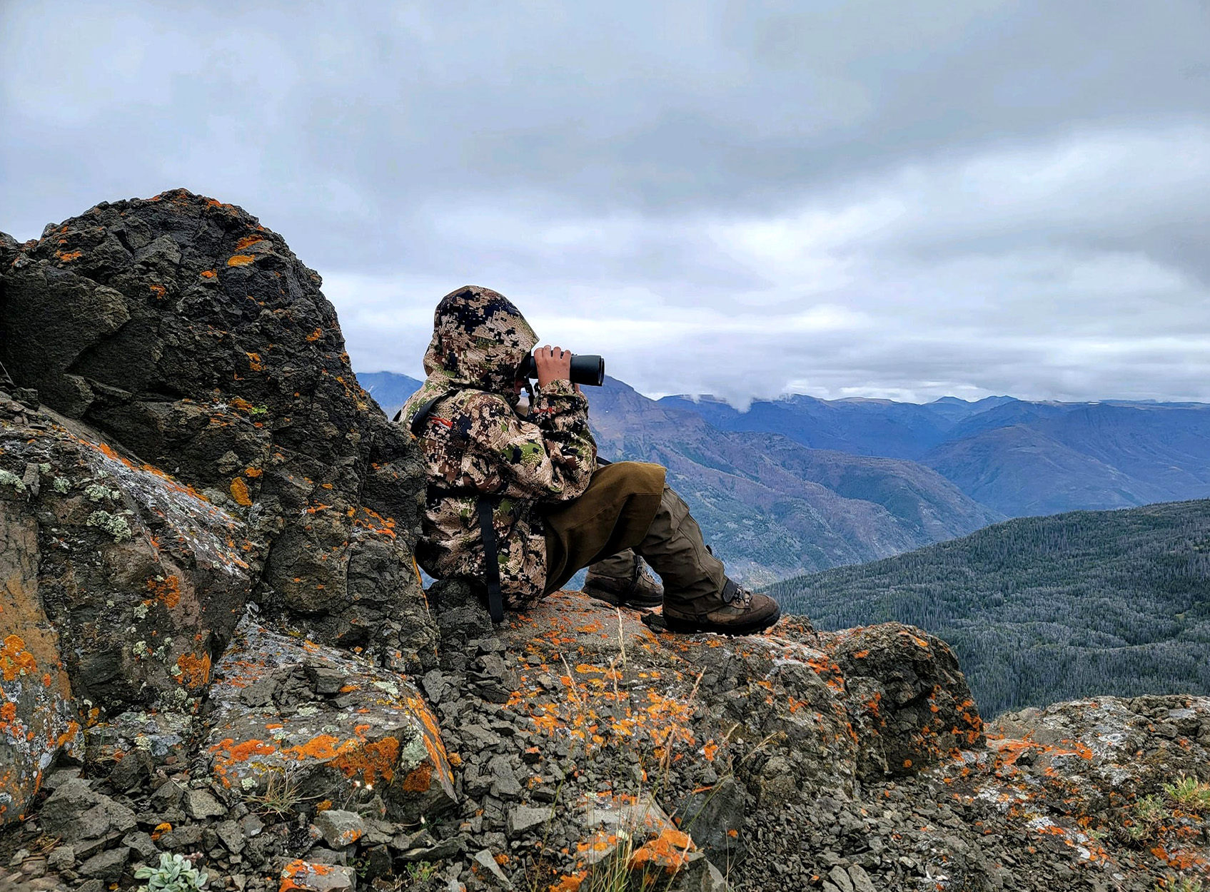 A young hunter glasses for game in the mountains.