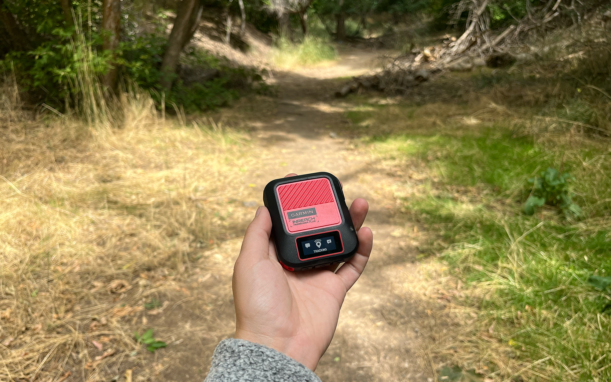 Hiker holds Messenger Plus device on trail.