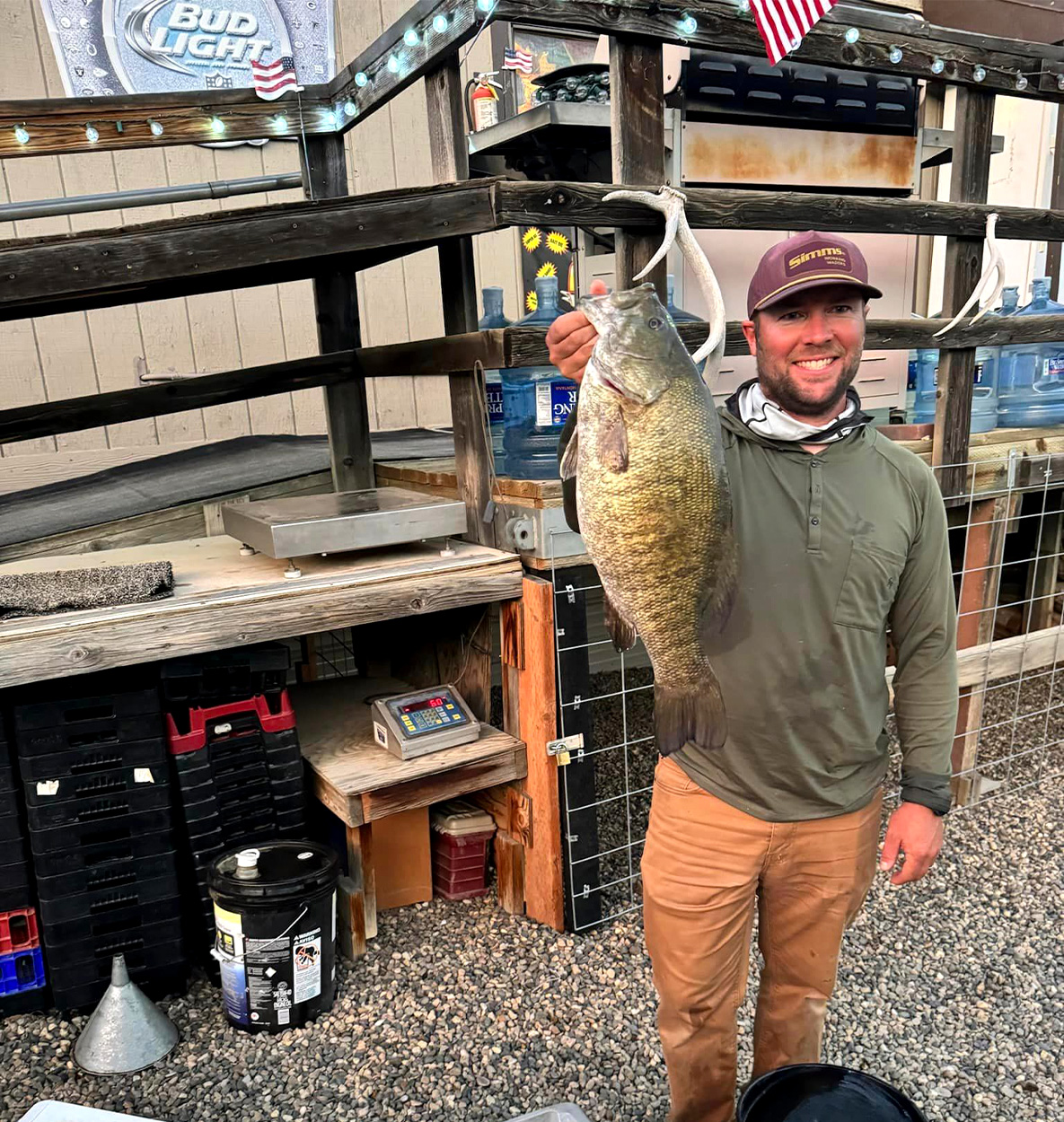 An angler holds up a smallmouth bass after weighing it.