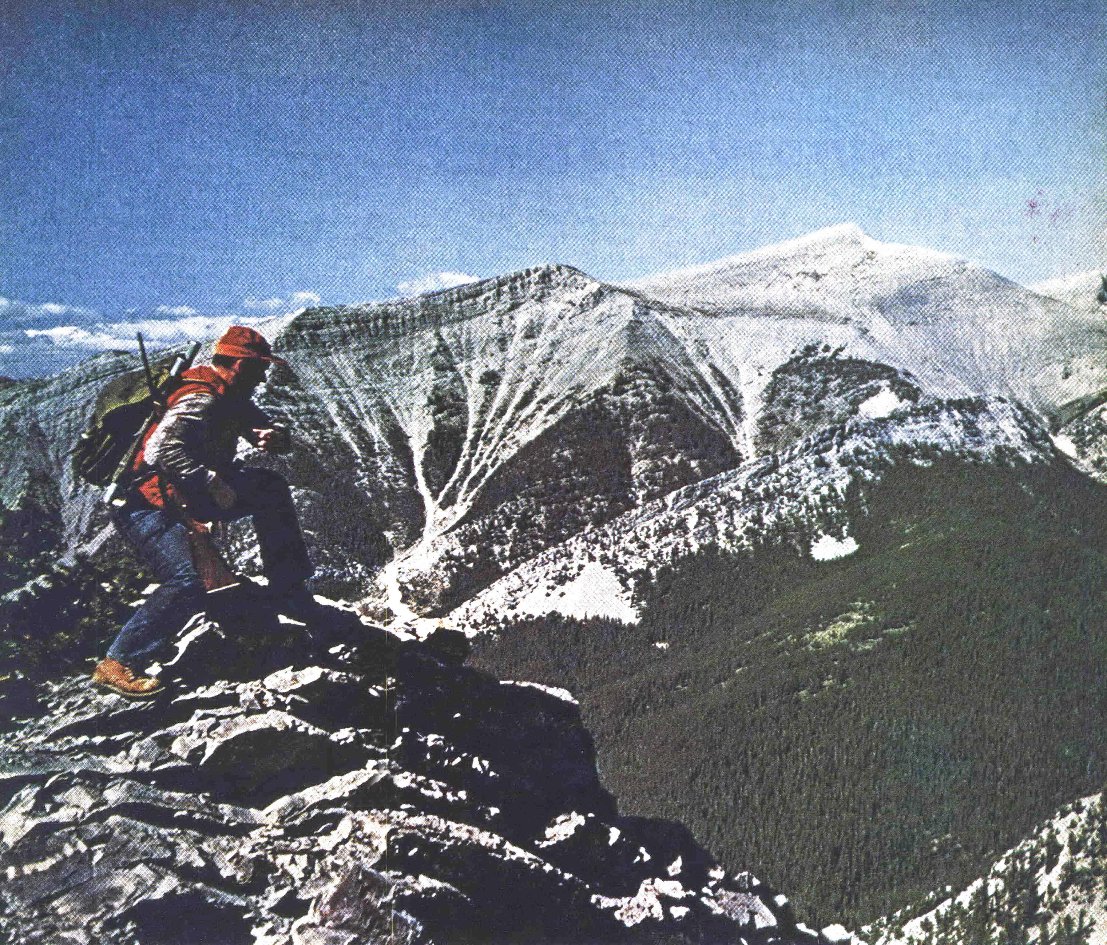 A hunter in an old photo kneels on a mountain ridge