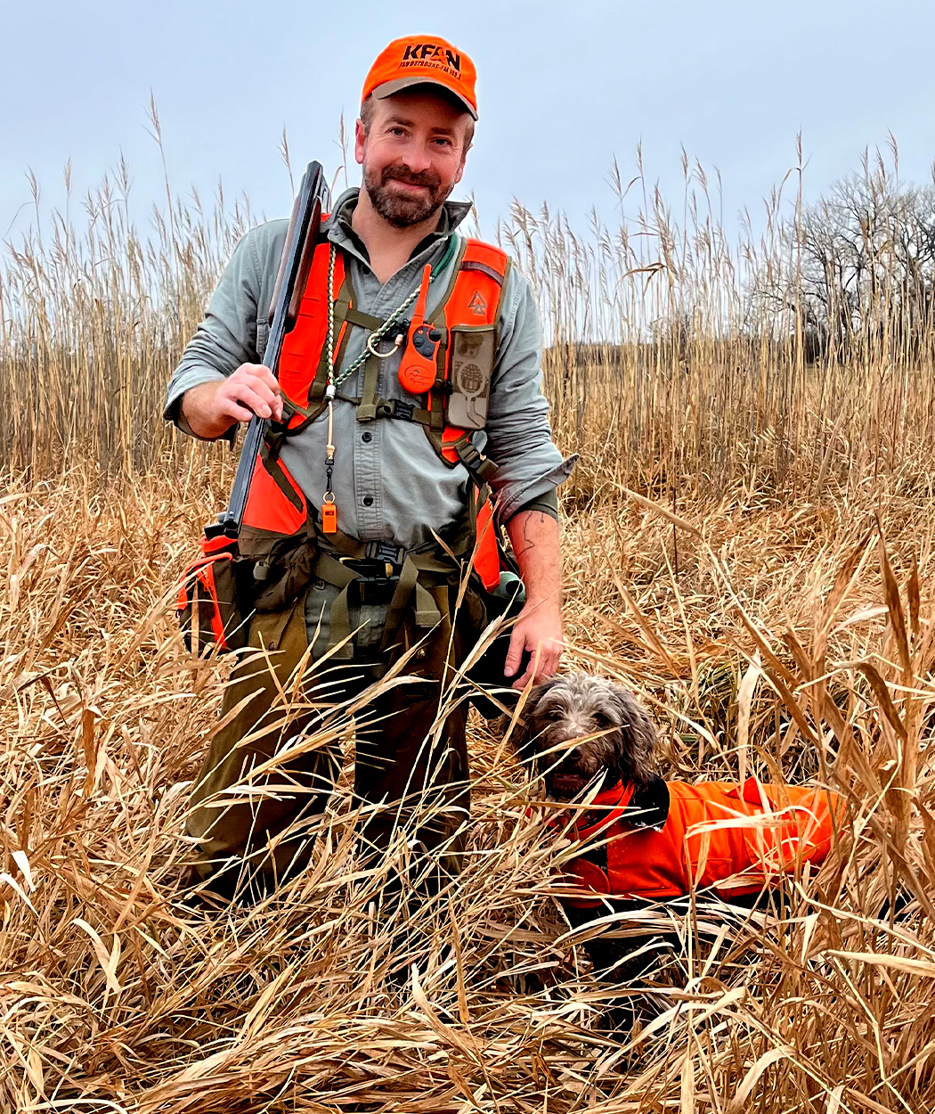 A pheasant hunter and his dog in a field of tall grass.