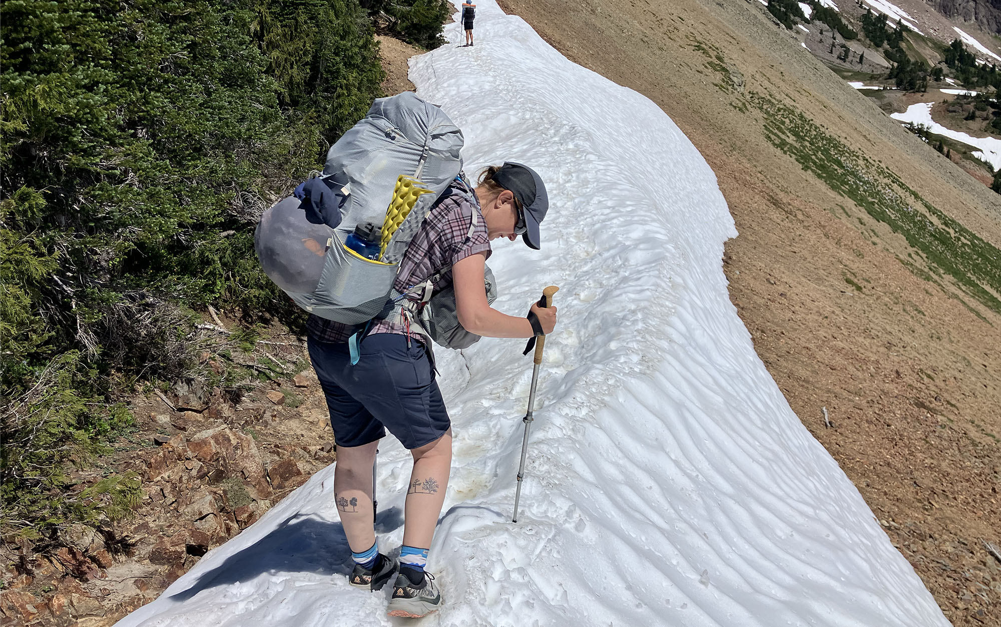 Woman walking across a ridge of snow with trekking poles while wearing the Aarn Mountain Magic 50 Pro