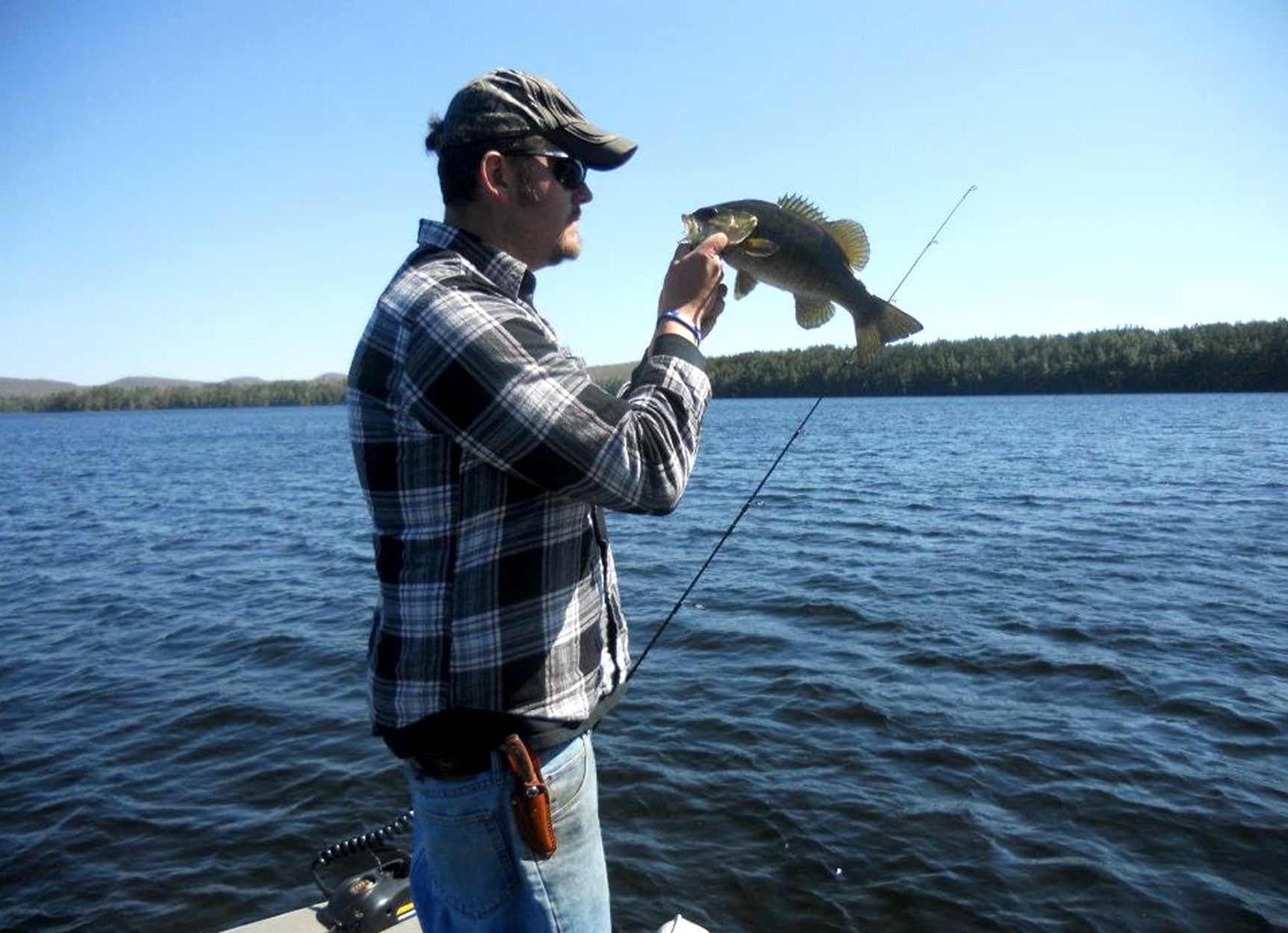 An angler holds up a smallmouth bass on a lake.