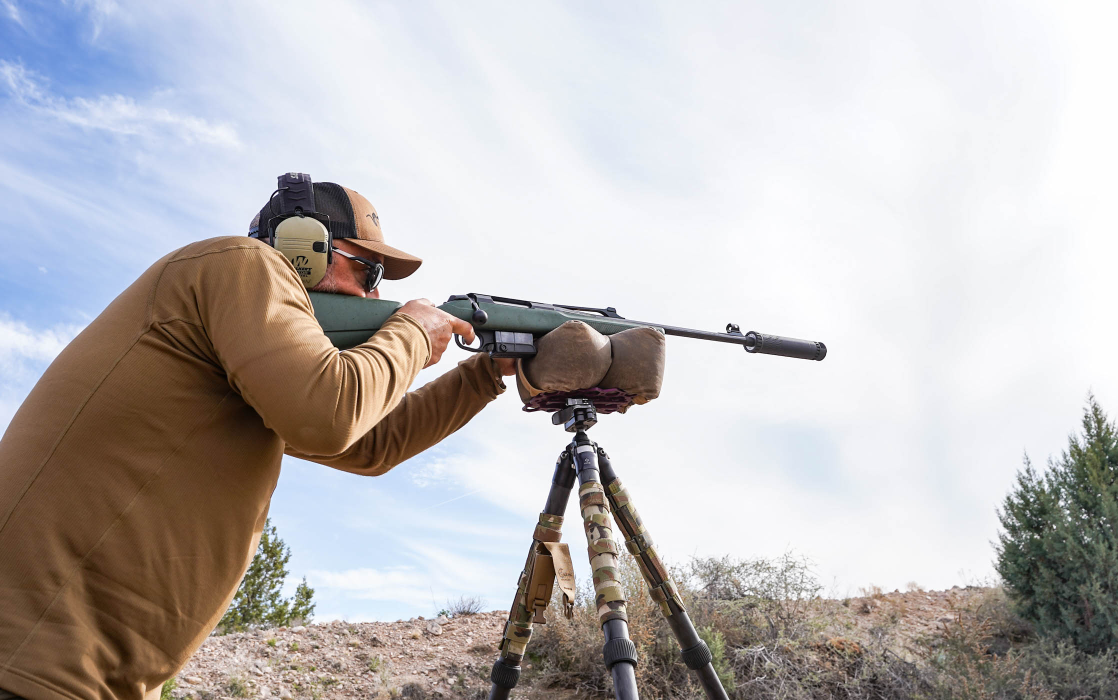 A hunter shoots a suppressed rifle of a tripod and shooting bag.