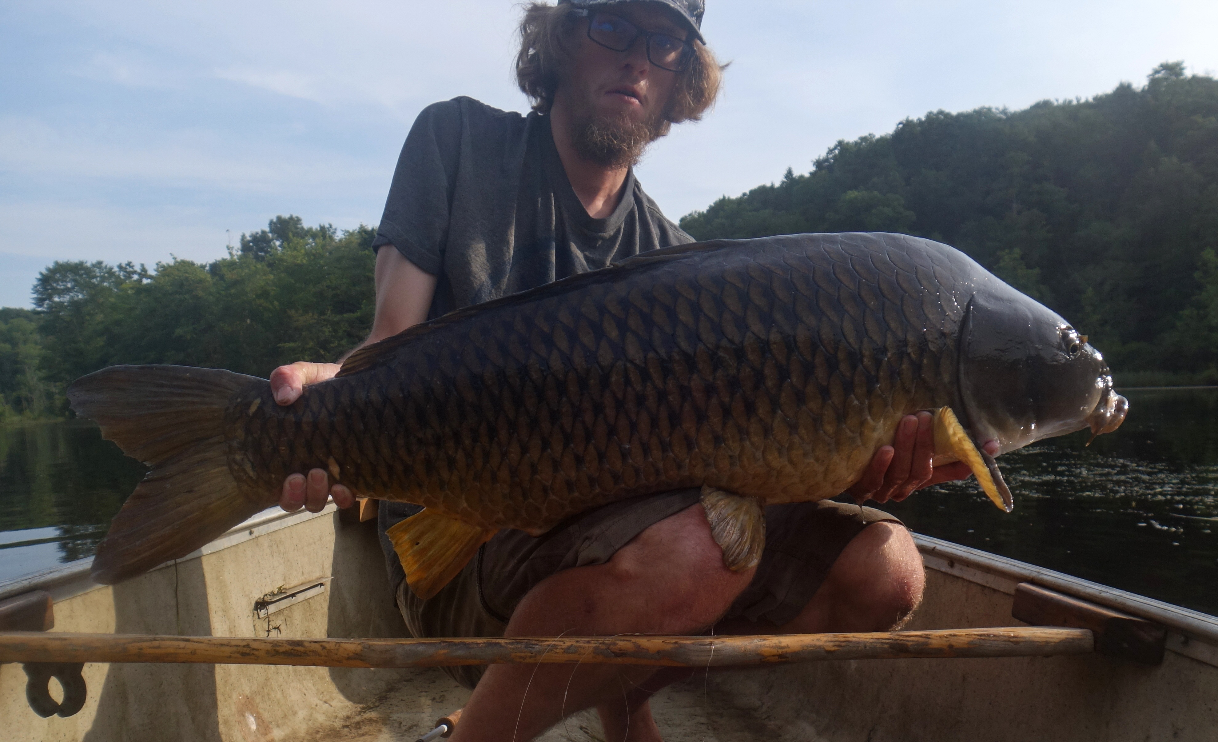 A man holds a big carp in a boat on the river.