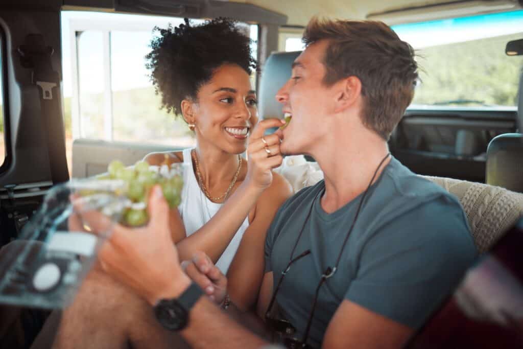 A couple in an RV feeding grapes from the farmers market to one another.