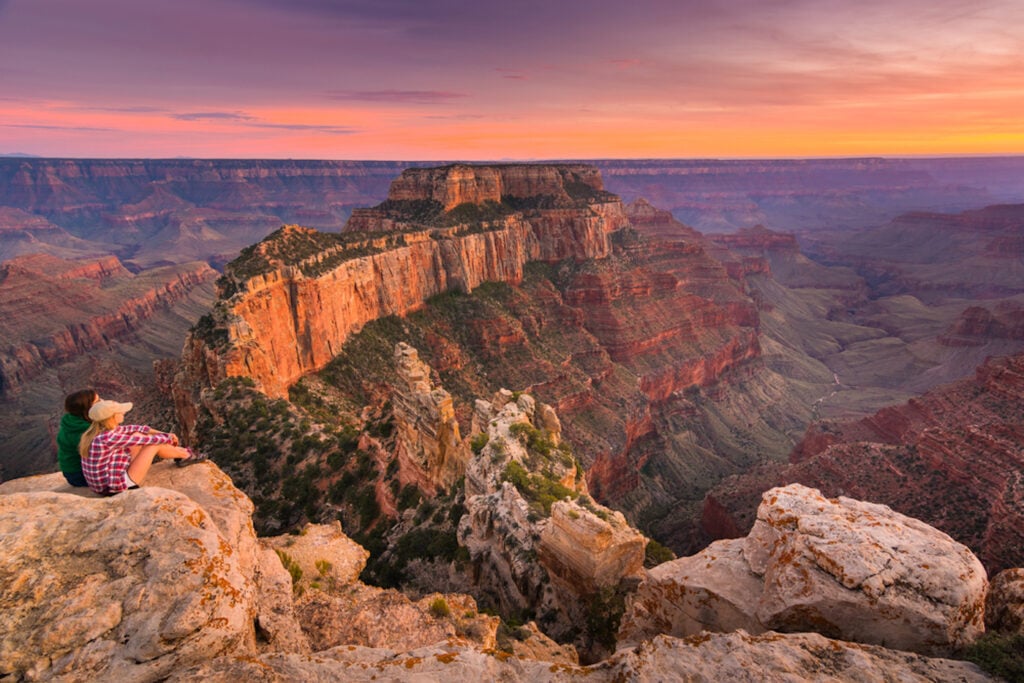 A couple looks out over teh Grand Canyon.