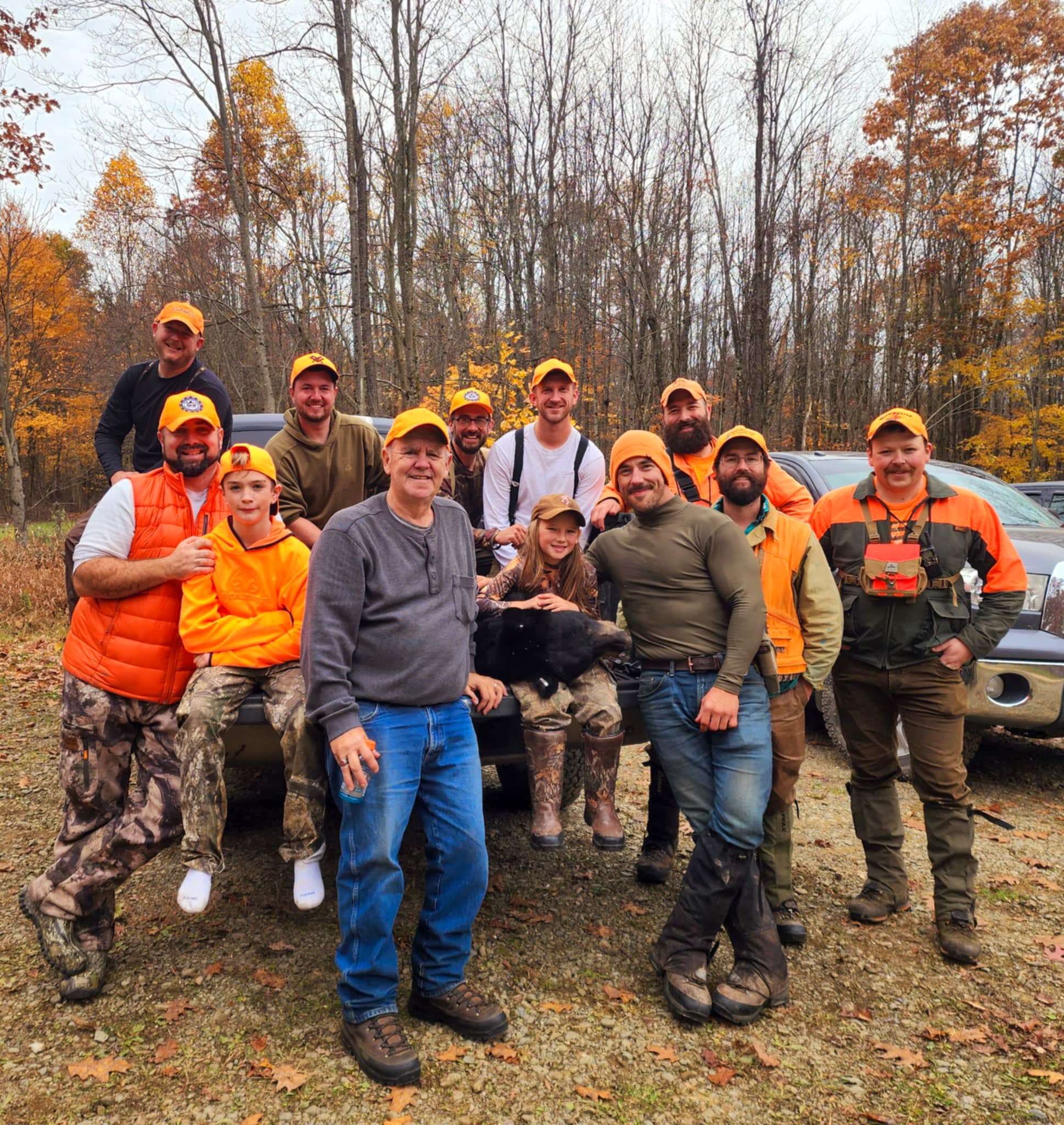 A bunch of hunters in blaze orange with a hunter and a bear on the tailgate.