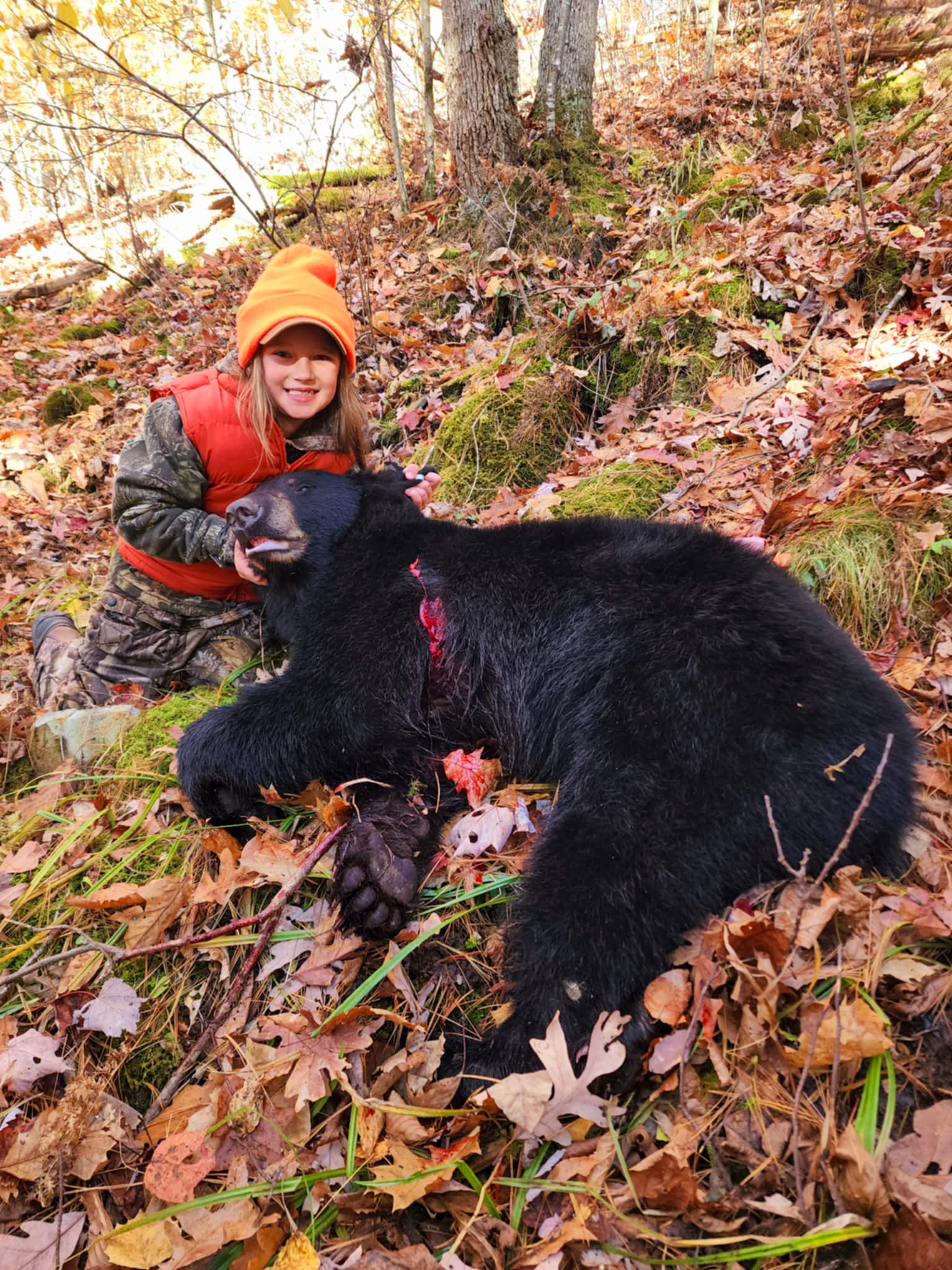 A young hunter in orange kneels besides a black bear.