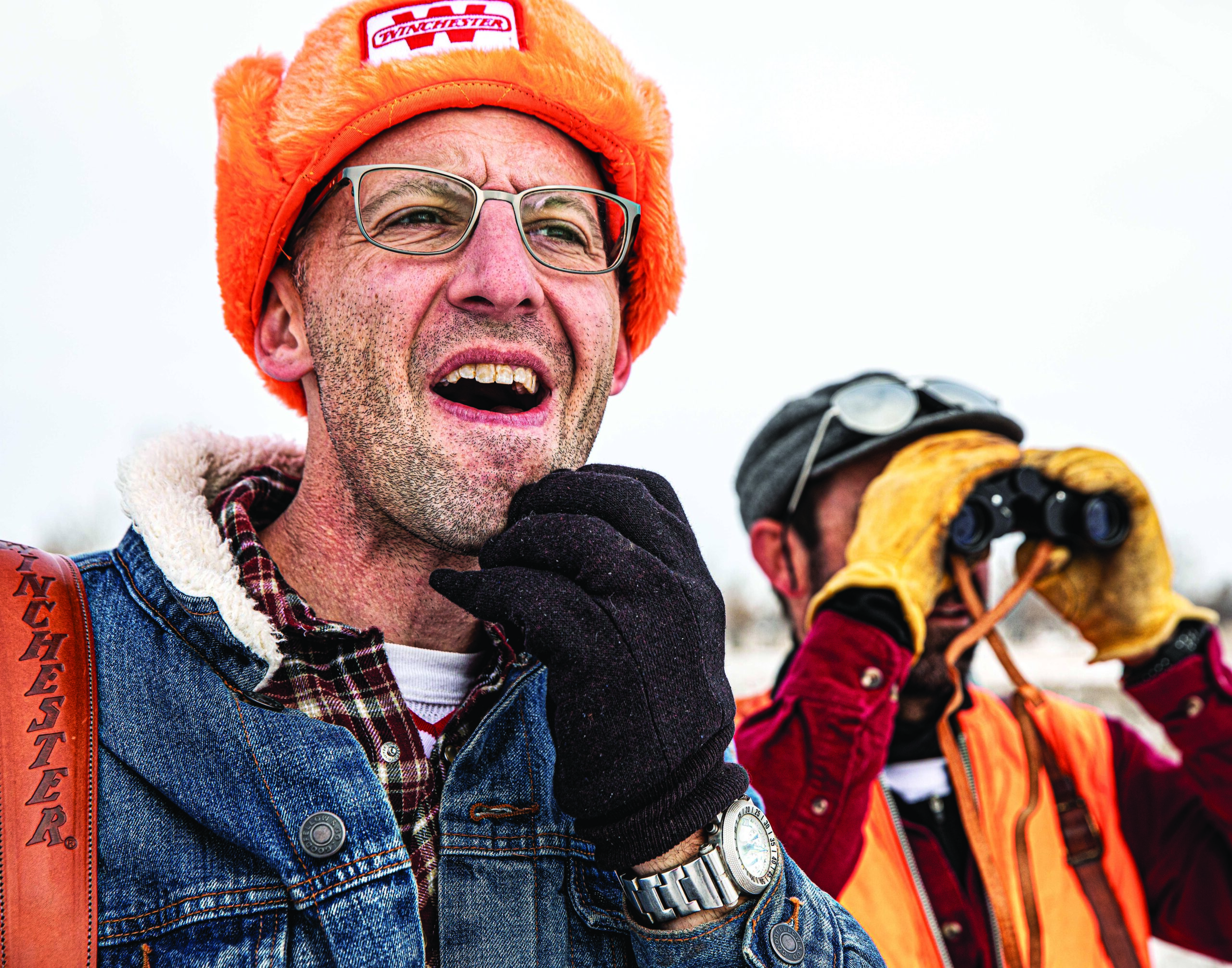 Two hunters in denim and blaze orange side by side looking for deer.