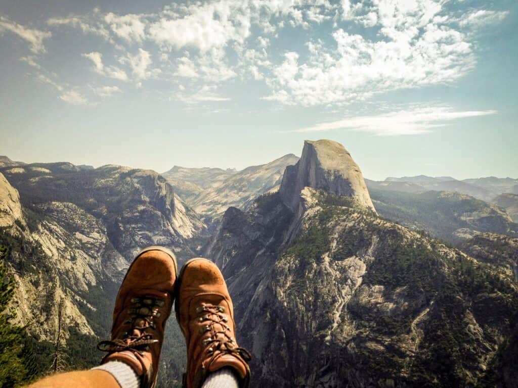 A hiker looks at Half Dome with his boots in the foreground.